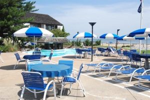 A pool with blue and white umbrellas, chairs and tables.