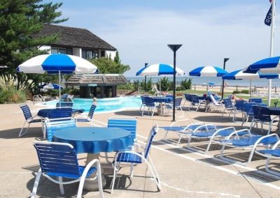 A pool with blue and white umbrellas, chairs and tables.