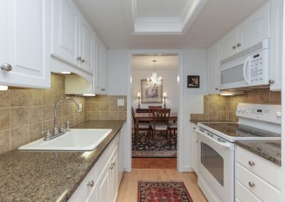 A kitchen with white cabinets and brown granite counter tops.