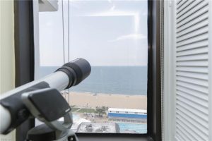 A telescope looking out of the window at the beach.