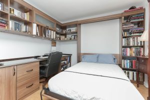 A bed with a desk and bookshelf in the corner