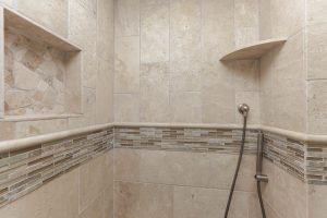 A shower with two tiled shelves and a hand held shower head.