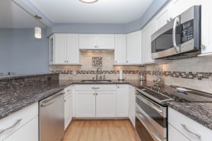 A kitchen with white cabinets and black counter tops.