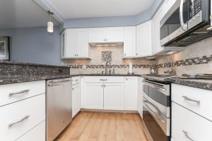 A kitchen with white cabinets and wood floors.